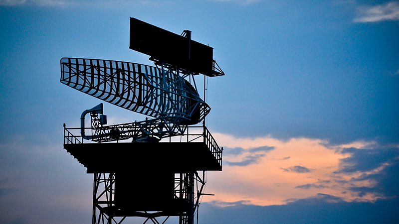 Broadcast radar tower silhouetted against a bright sky